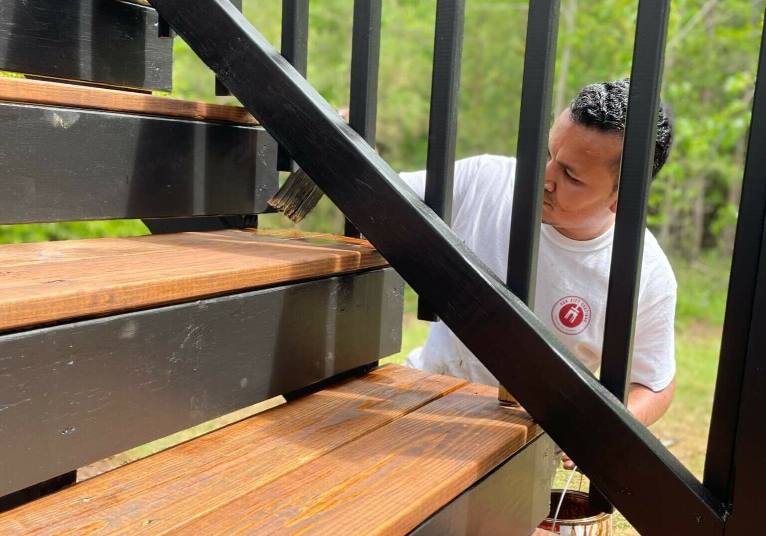 A worker applying a coating to wooden deck stairs, from Oak City's deck-stain guide